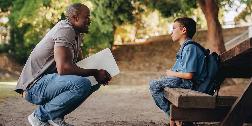 adult-talking-with-youth adult speaking with young man while sitting on a bench
