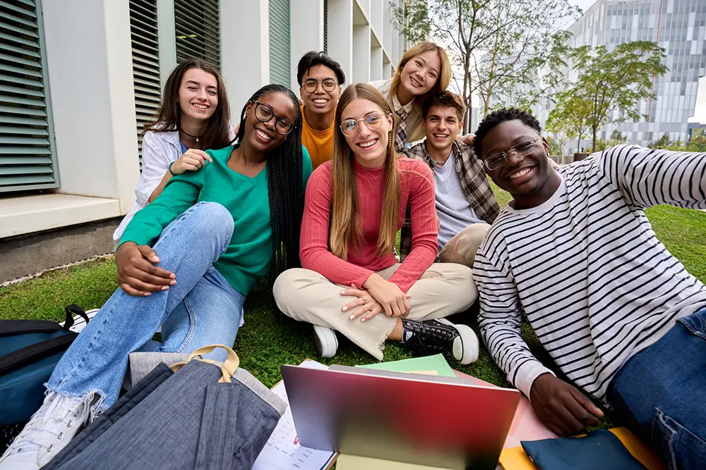 photo of young adults siting in grass smiling